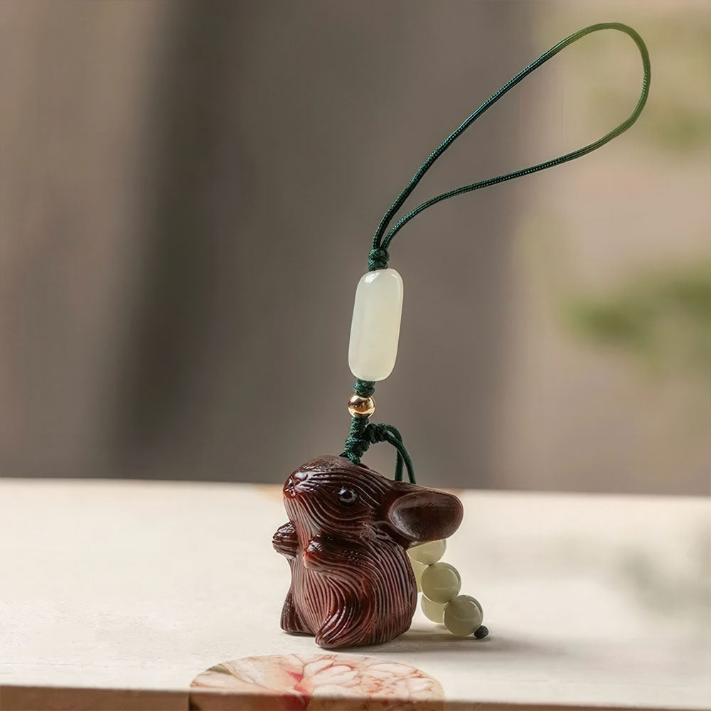 Le porte-bonheur lapin en bois foncé avec son cordon simple et ses perles de jade.
