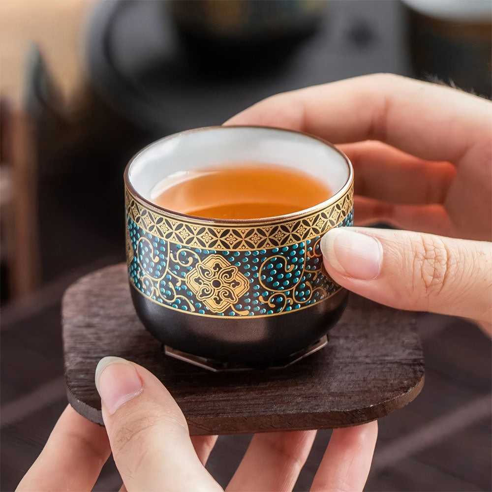 Tasse chinoise en porcelaine dorée tenue en main pour une dégustation de thé